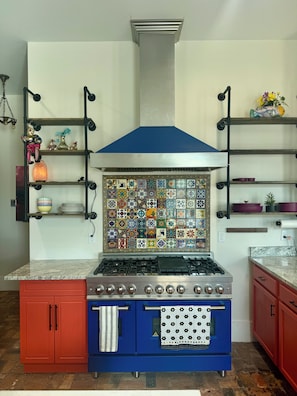 A kitchen with a blue stove, red cabinets, and a decorative tile backsplash.