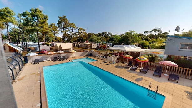 Ein Schwimmbecken mit Liegestühlen und Sonnenschirmen, umgeben von einer Terrasse und Bäumen.