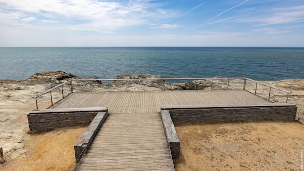 En træpromenade der fører til en stenet kystlinje med udsigt over havet.