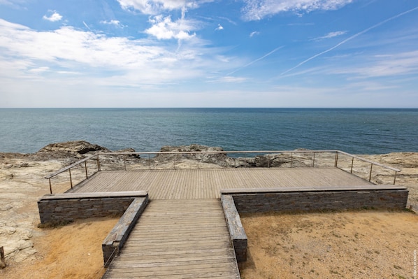 Ein hölzerner Steg führt zu einer felsigen Küstenlinie mit Blick aufs Meer.