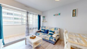 Ein Wohnzimmer mit einer Couch, einem Tisch, einem Sessel, einem Fenster mit Vorhängen und einem Bild an der Wand.