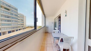 En balkon med udsigt til en moderne bygning, et hvidt bord og to hvide stole.