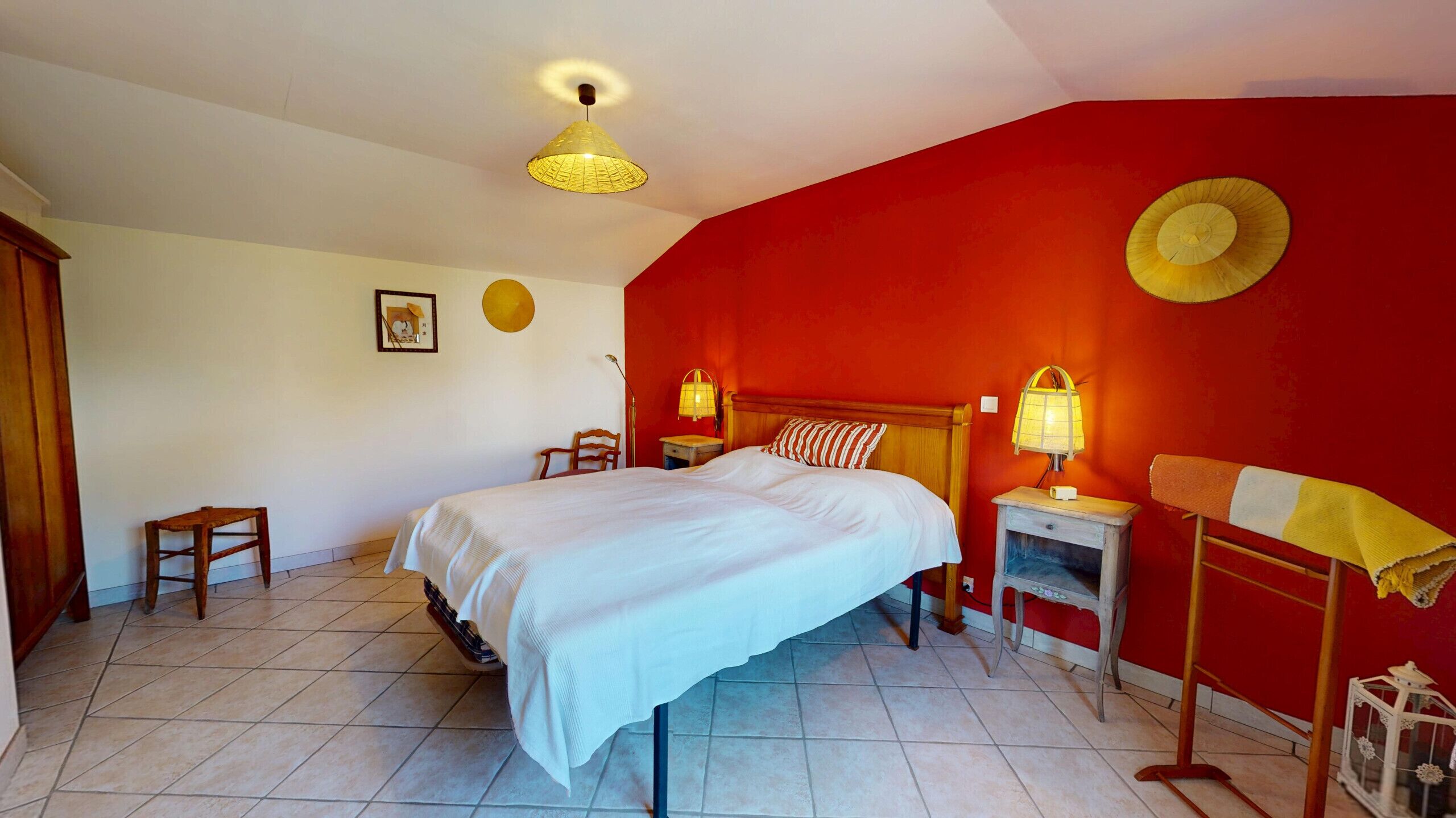 Ein Schlafzimmer mit einem Bett, zwei Nachttischen mit Lampen, einem Sessel, einem kleinen Tisch und einer roten Wand.