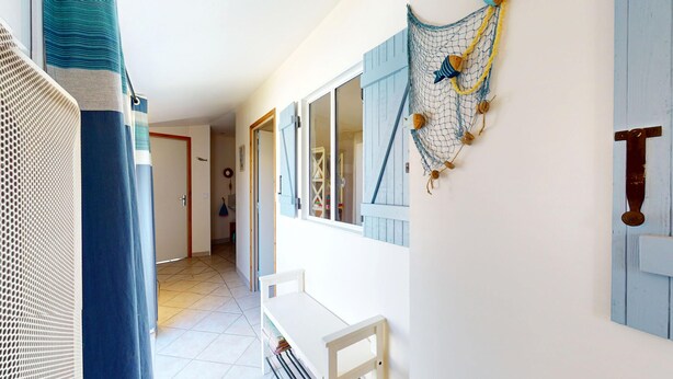 Een hal met een witte bank, een decoratie van een net met houten vissen, en een deur met blauwe luiken.