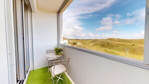 Un balcon donnant sur un paysage verdoyant, une petite table avec une plante et une chaise pliante.