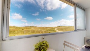 A room with a large window overlooking a grassy landscape with a clear sky. - Le Spot des Becs (Saint-Hilaire-de-Riez)