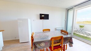 Un espace repas comprenant une table, des chaises, un téléviseur fixé au mur, un réfrigérateur et une vue sur l’extérieur.