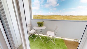 Un balcon avec une petite table et deux chaises, un pot de fleurs et une vue sur un paysage verdoyant.