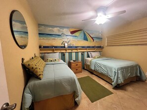 A bedroom with two beds, a ceiling fan, a beach-themed mural, and a wooden dresser. - VAN LEE BEACH CONDO 204!!!! (Ormond Beach)