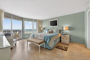 A bedroom with a bed, a bench, a nightstand, a TV, and a view of the sea. - VAN LEE BEACH CONDO 204!!!! (Ormond Beach)