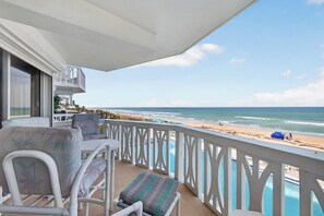 Un balcón con barandillas blancas, una piscina y vista a la playa.
