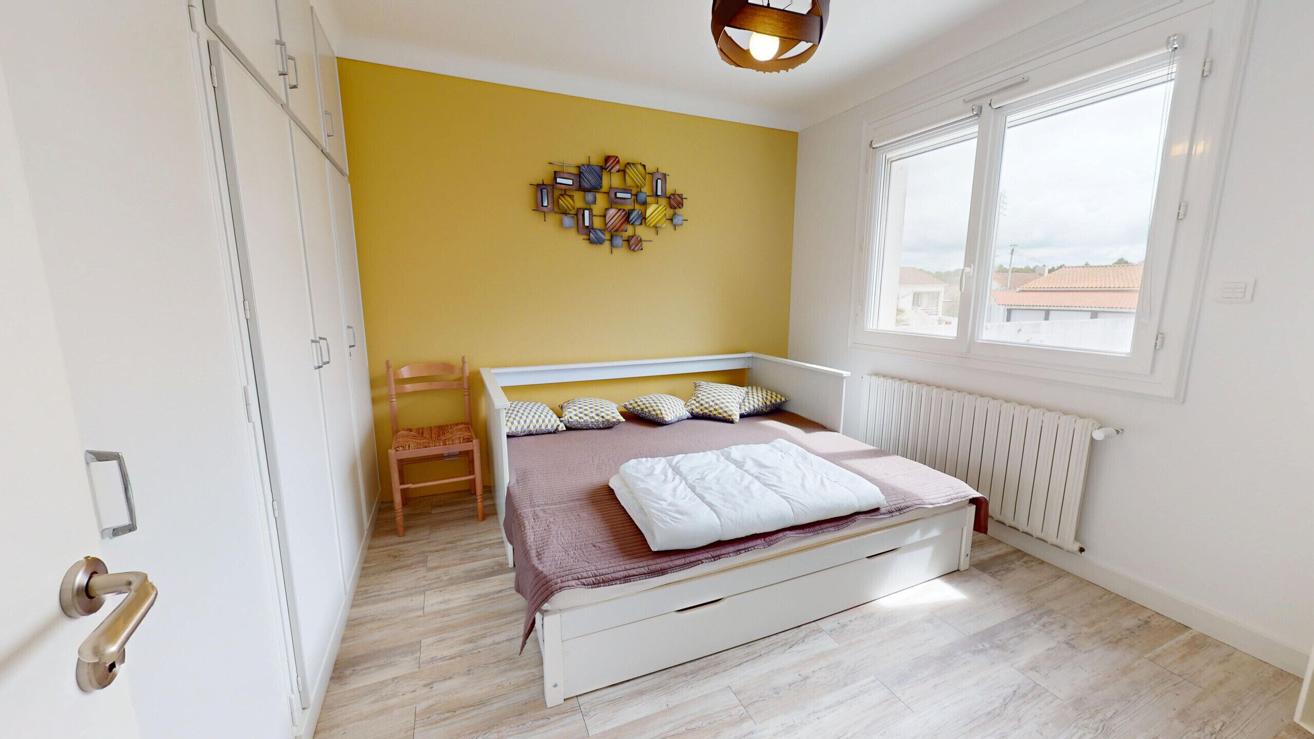 A bedroom with a bed, a chair, a radiator, and a window with a view.