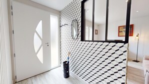 Un couloir avec un mur orné d’un motif géométrique, une porte avec une découpe en forme de losange et une poubelle.