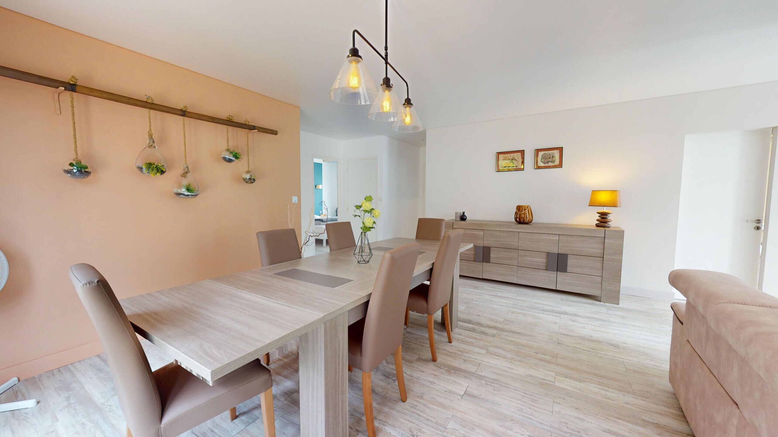 A modern dining area with a wooden table and chairs, a hanging light fixture, and a minimalist decor.