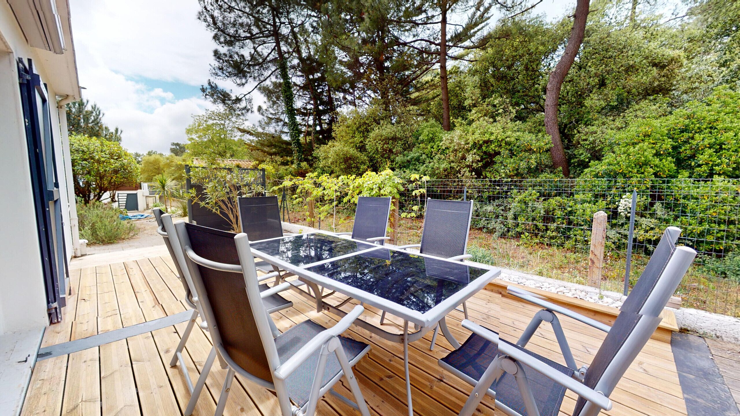 Eine Terrassenausstattung im Freien mit einem Glastisch und Metallstühlen, umgeben von einem Holzboden und einem Drahtzaun.