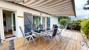 Une terrasse extérieure couverte, dotée d’une table et de chaises, d’une plateforme en bois et offrant une vue sur le jardin environnant.