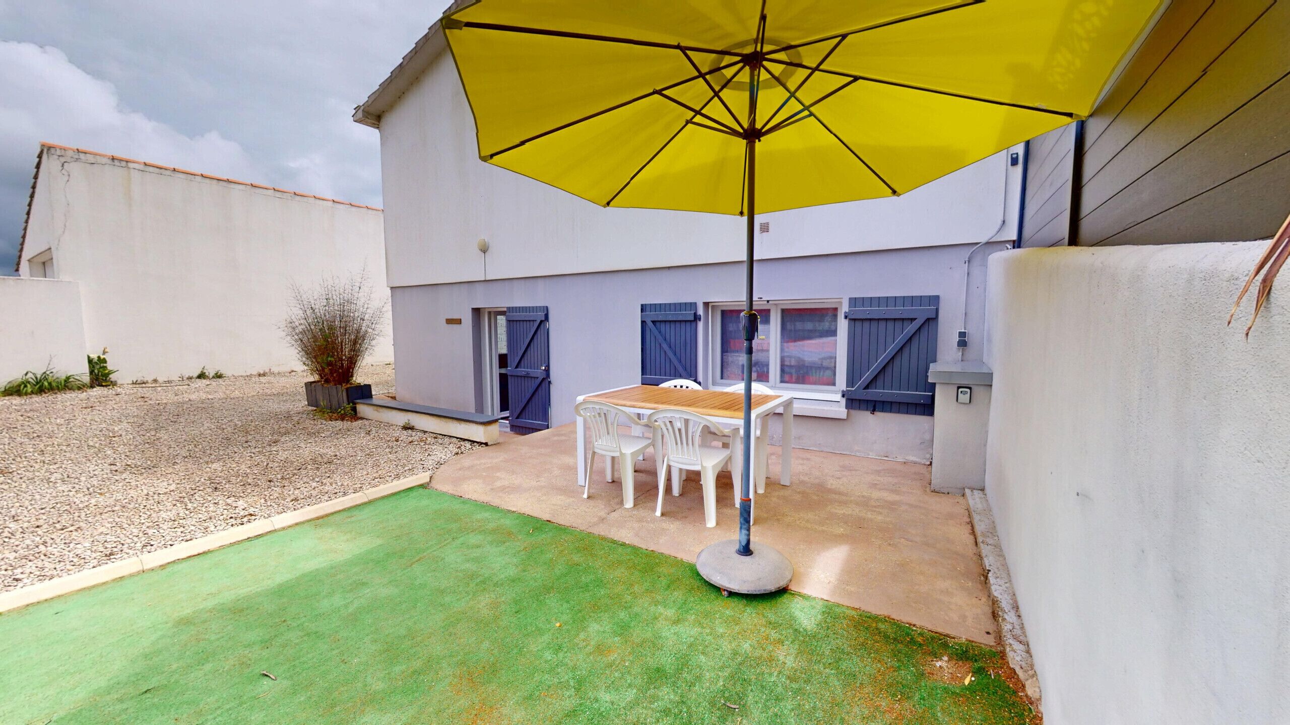 A patio with a table and chairs, a yellow umbrella, and a small garden area.