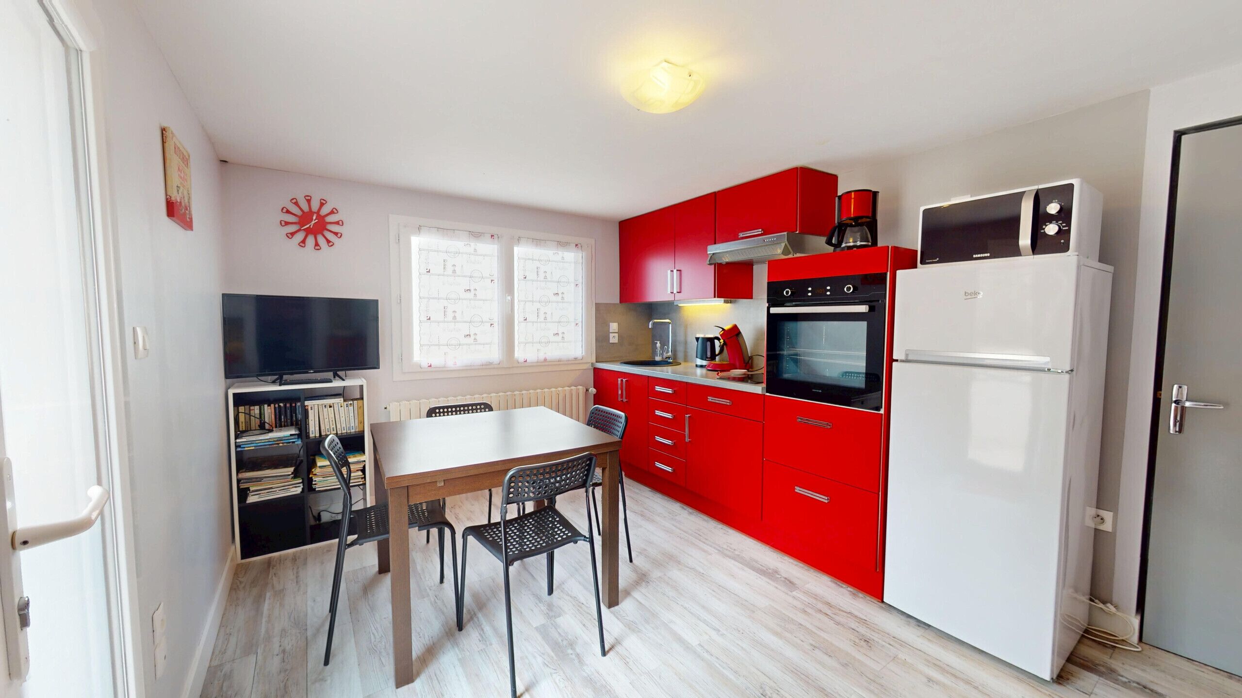 Une cuisine de taille réduite avec des meubles rouges, un réfrigérateur blanc, un four noir et une table à manger avec des chaises.