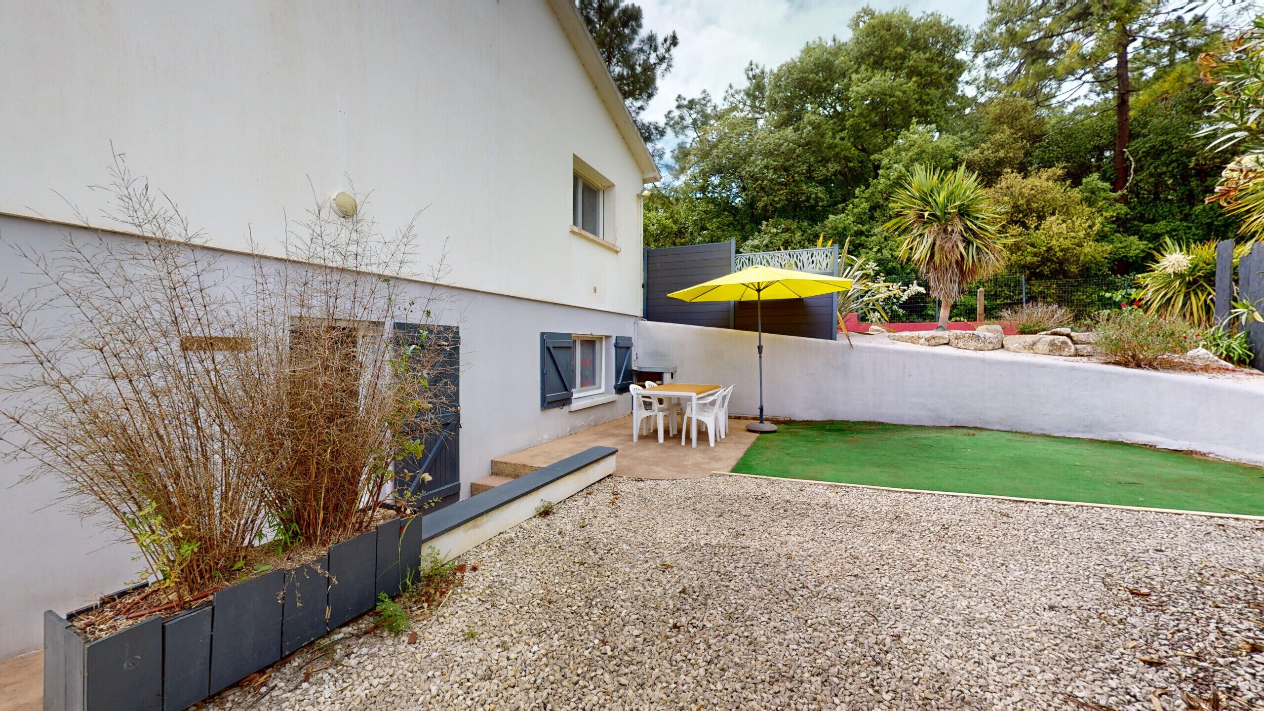 Une maison moderne dotée d’un patio, d’une petite table avec des chaises et d’un parasol jaune.