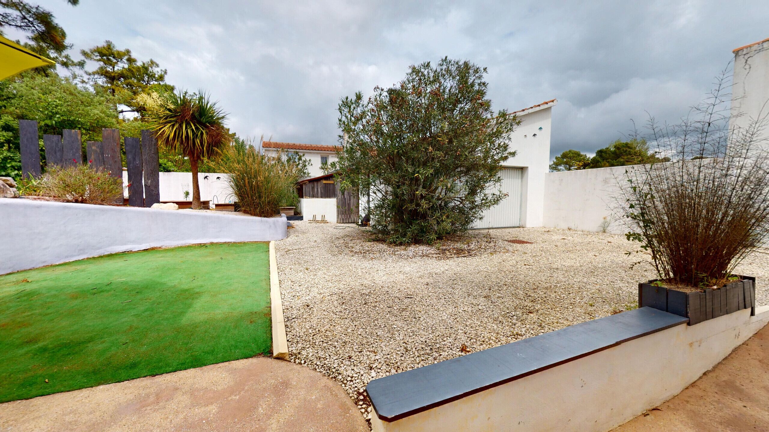 A residential area with a green lawn, gravel path, and a white building with a red roof.