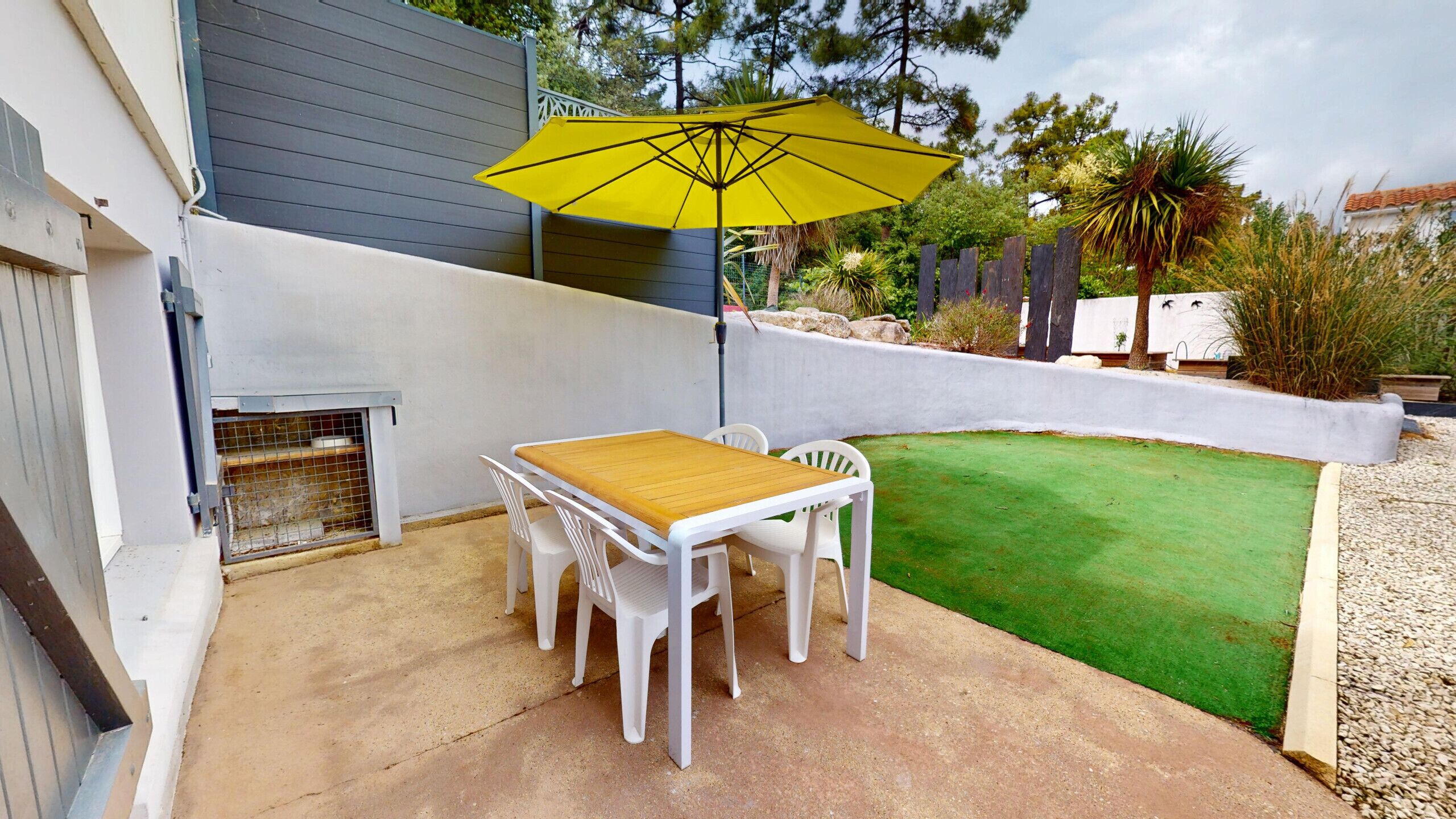 A patio with a table and chairs, a yellow umbrella, and a small lawn.
