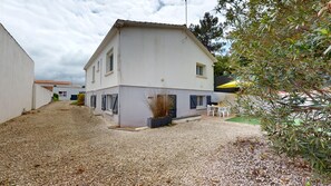 Ein zweistöckiges Haus mit Kiesweg und kleiner Terrasse, ausgestattet mit Gartenmöbeln.