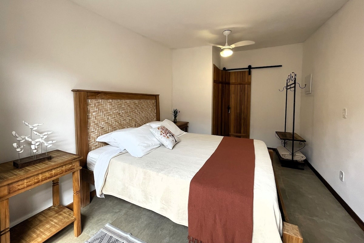 A bedroom with a bed, wooden headboard, bedside table, and a ceiling fan.