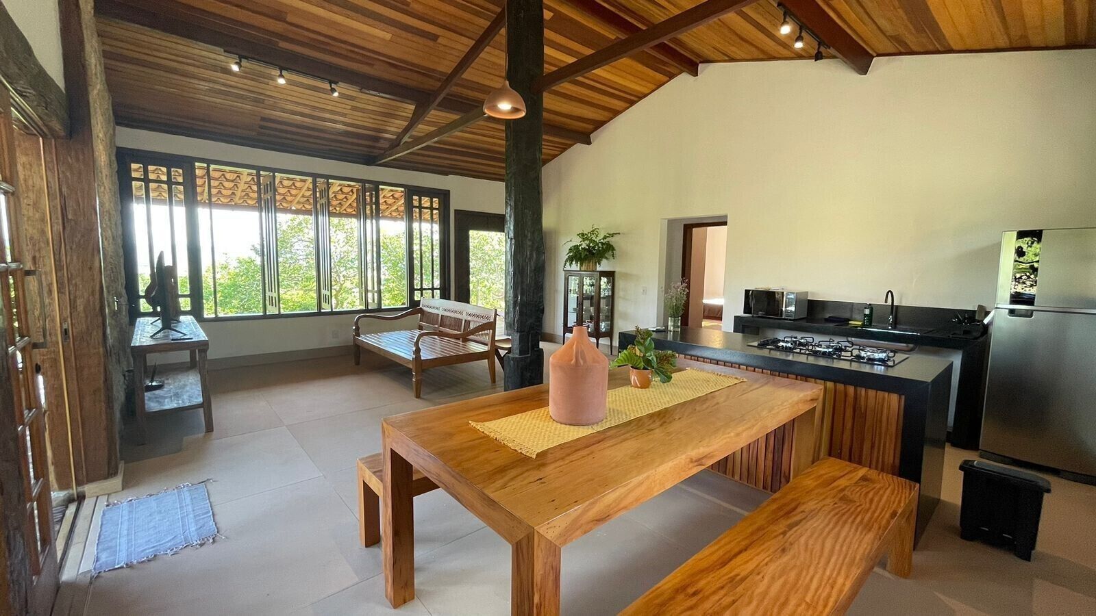A spacious kitchen with a wooden table, bench, and a view of the outdoors through large windows.