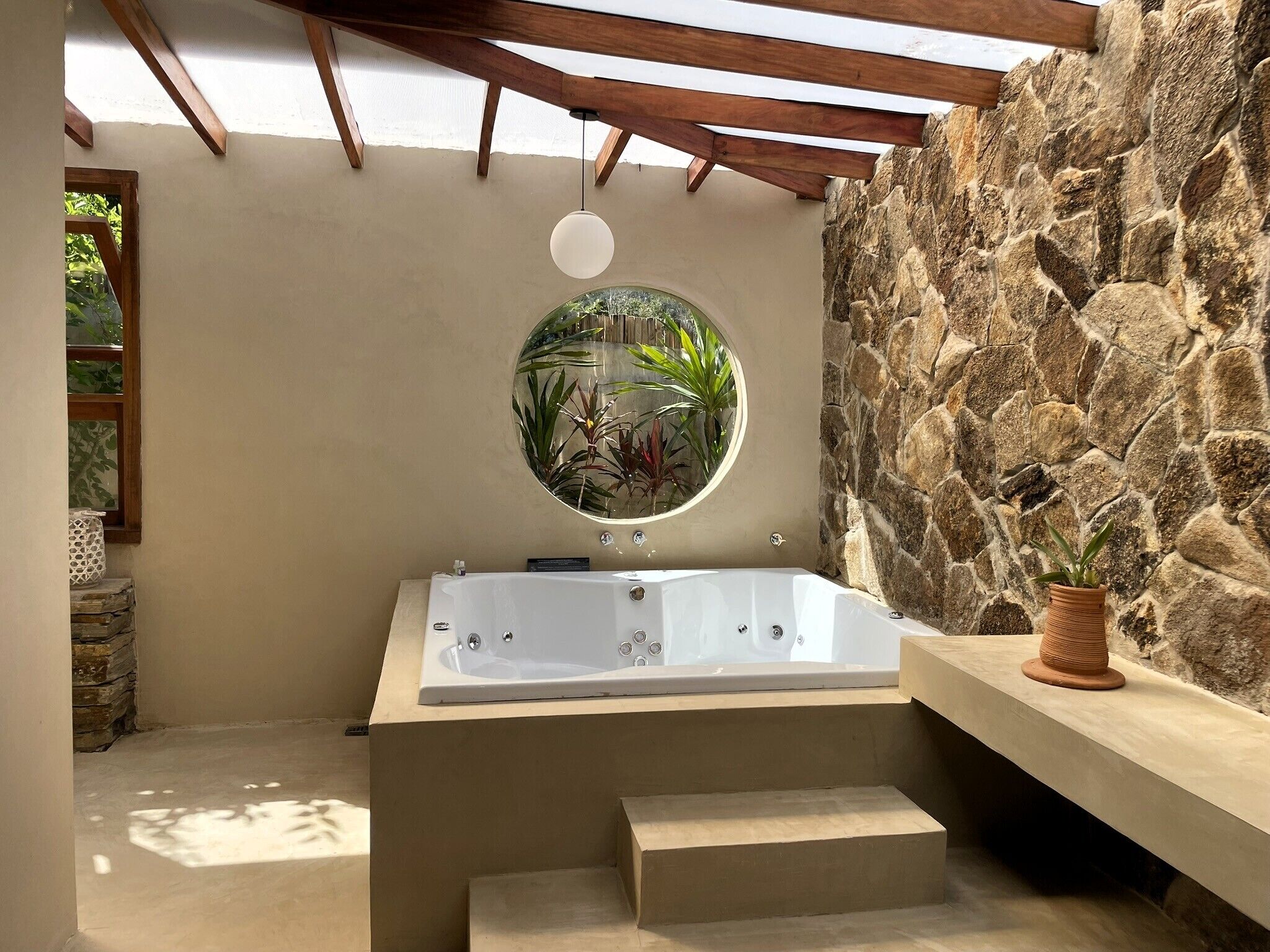 A modern bathroom with a freestanding bathtub, a stone wall, and a circular mirror.