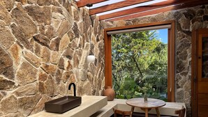 Uma parede de pedra, uma pia, uma mesa com cadeiras e uma porta.