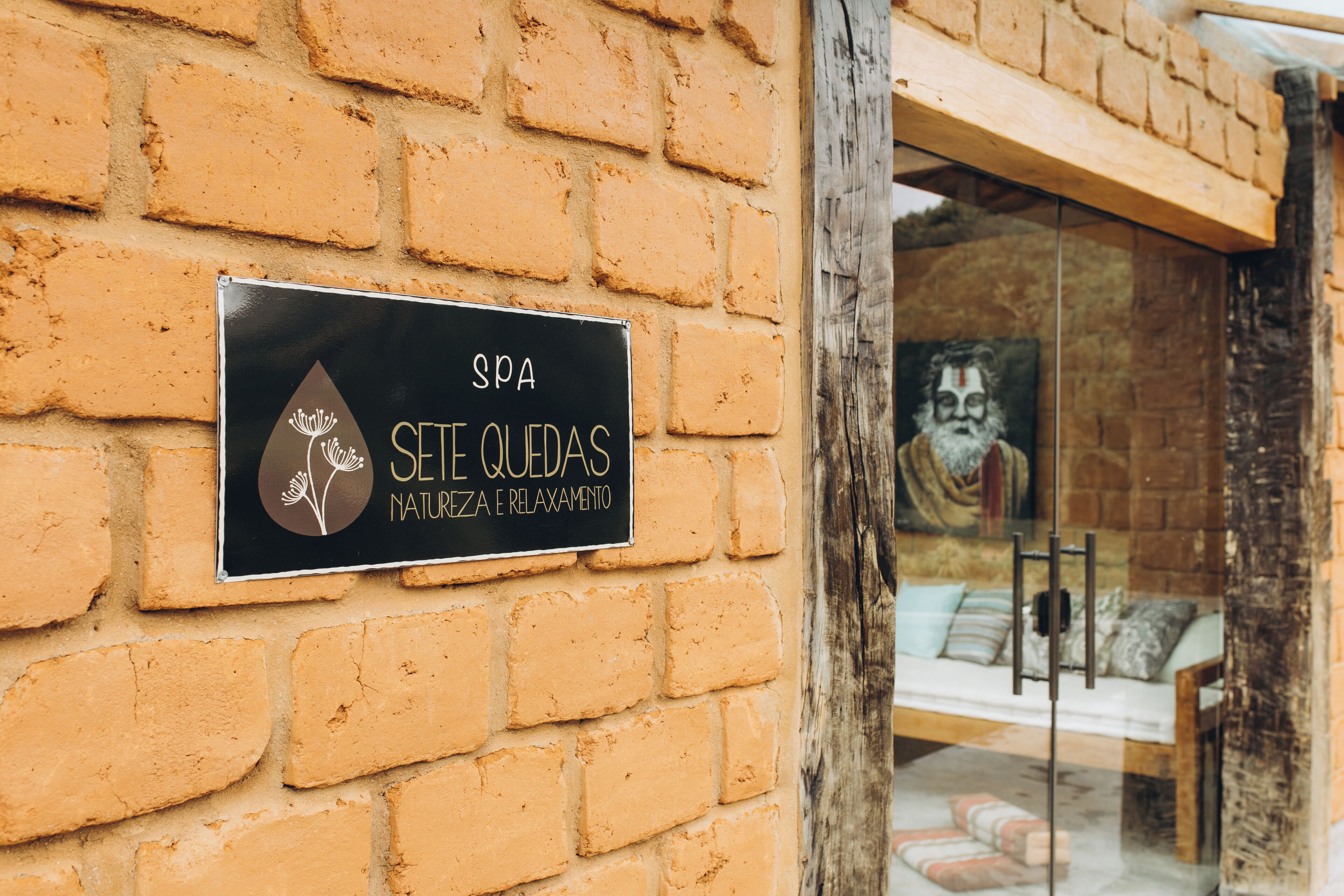 A spa sign on a brick wall, a glass door, and a glimpse of a room with a bed and pillows.