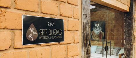 A spa sign on a brick wall, a glass door, and a glimpse of a room with a bed and pillows.