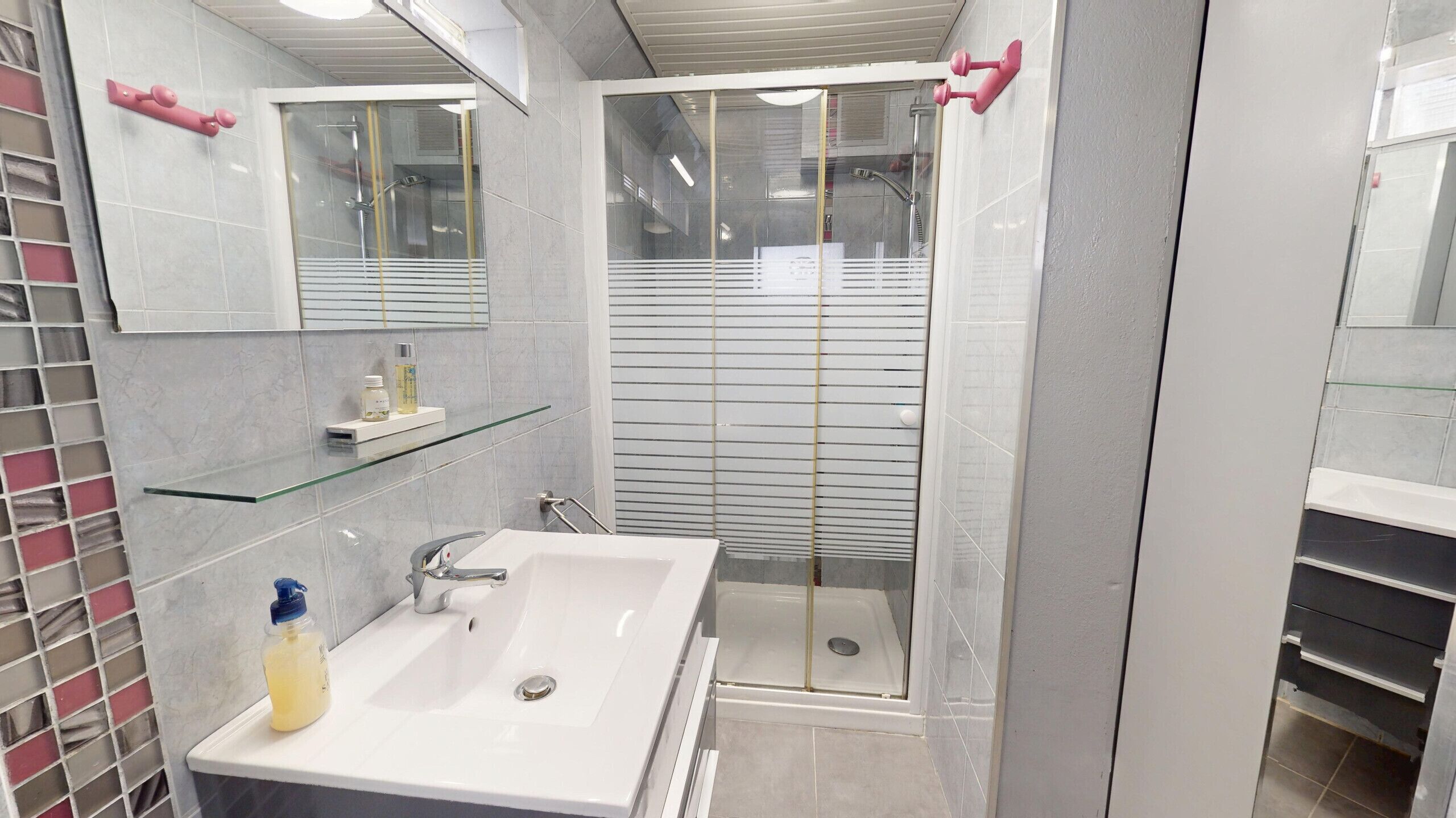 A modern bathroom with a glass shower enclosure, a white sink, and a mirror above it.