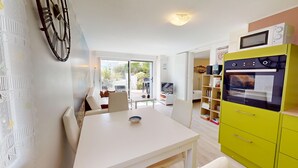 A modern kitchen with a white table and yellow cabinets, a TV, and a bookshelf. - Dune - Apartment 40m² with Terrace (La Barre-de-Monts)