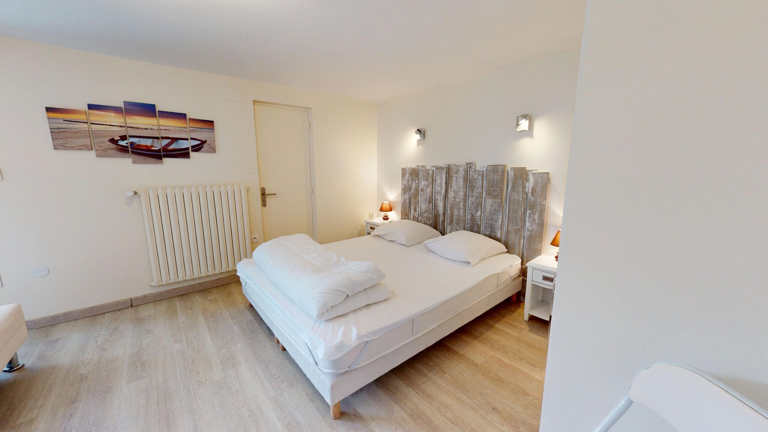 Un dormitorio con cama, mesitas de noche, radiador, puerta y un cuadro colgado en la pared.