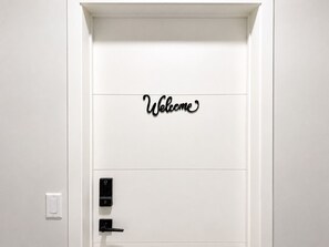 Eine weiße Tür mit einem 'Welcome'-Schild und einem modernen elektronischen Schloss.