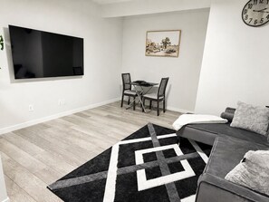 Ein modernes Wohnzimmer mit Flachbildfernseher, einem Esstisch mit Stühlen, einer Couch und einem gemusterten Teppich.
