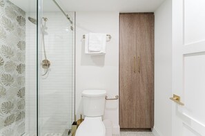 Ein Badezimmer mit Duschkabine aus Glas, Toilette, Handtuchhalter und einem Holzschrank.