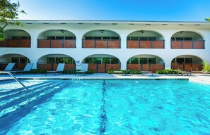 Ein Schwimmbecken mit Liegestühlen und ein Gebäude mit Rundbogenfenstern.