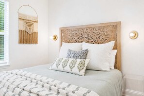 Een slaapkamer met een bed, hoofdeinde, een wandspiegel en een wandlamp.