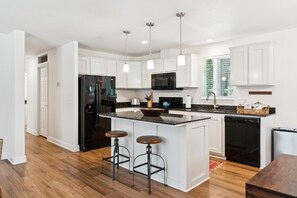 A modern kitchen with white cabinets, a black refrigerator, a microwave, and a dishwasher. There are two bar stools at the island. - The Arbordale: 9-Acre, Redwoods, Secluded (Sebastopol)