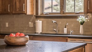 Cucina con mobili in legno, piano di lavoro in granito, lavello in acciaio inossidabile e finestra vista alberi.