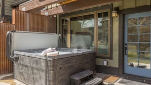Una vasca idromassaggio dall'atmosfera rilassante, con una panca, un bicchiere e un asciugamano, all'esterno di una casa con un patio in legno e una porta a vetro.