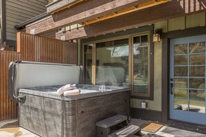 Ein Whirlpool im Wellness-Stil mit Sitzbank, einem Glas und einem Handtuch, vor einem Haus mit Holzterrasse und Glastür.