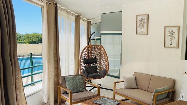 A modern living room with a hanging chair, sofa, and coffee table, large windows with curtains, and framed artwork on the wall. - Le cocon de Sète - patio+pool and beach on foot (Sète)