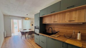A modern kitchen with wooden cabinets, a black sink, and a dining area with a table and chairs. - Le cocon de Sète - patio+pool and beach on foot (Sète)