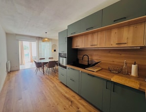 A modern kitchen with wooden cabinets, a black sink, and a dining area with a table and chairs. - Le cocon de Sète - patio+pool and beach on foot (Sète)