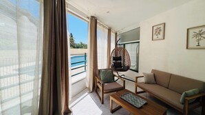 A living room with a hanging chair, a sofa, a coffee table, and a view of a pool through a window. - Le cocon de Sète - patio+pool and beach on foot (Sète)