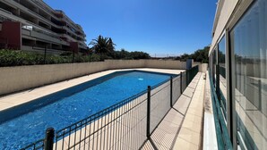 A swimming pool with a metal fence, a building with multiple balconies, and a clear blue sky. - Le cocon de Sète - patio+pool and beach on foot (Sète)