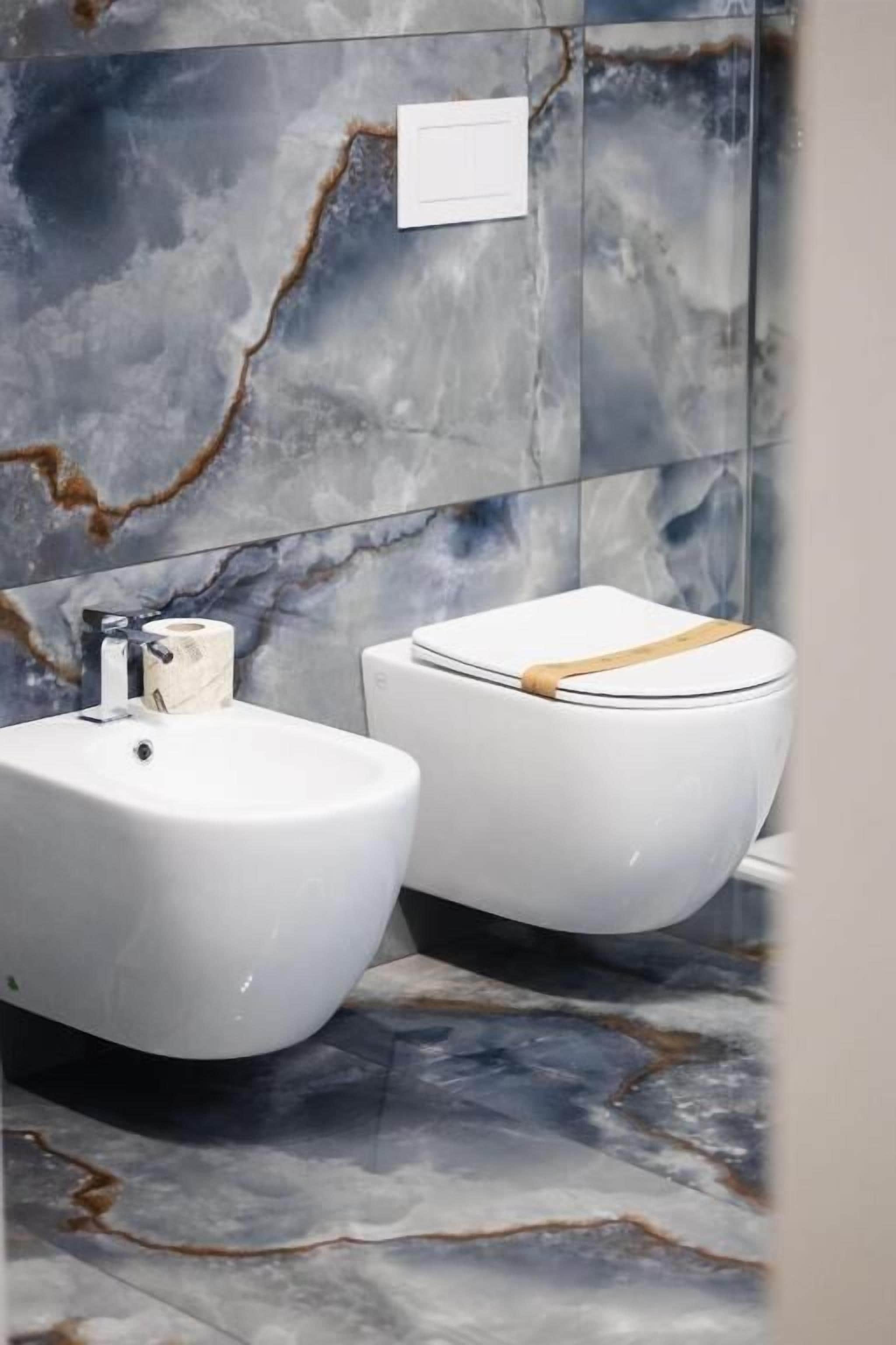A bathroom with a marble wall, a white sink, and a toilet.